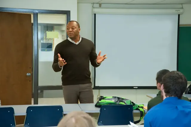 Kevin talking with students near a classroom projection screen